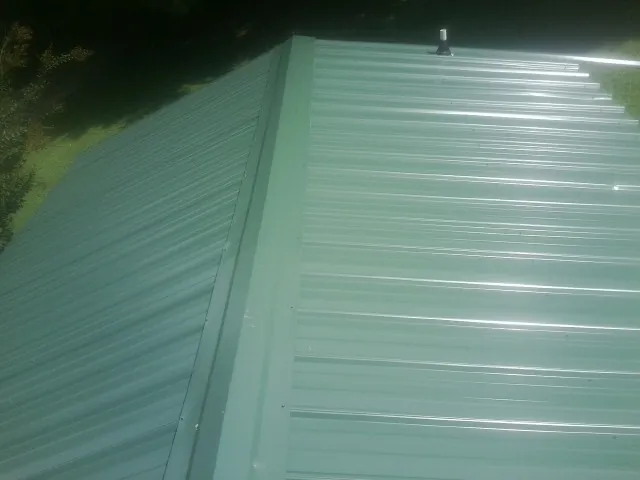 New green metal panels meeting at the ridge of a roof — Flat Roof Repair work by our crew in Ocean Gate