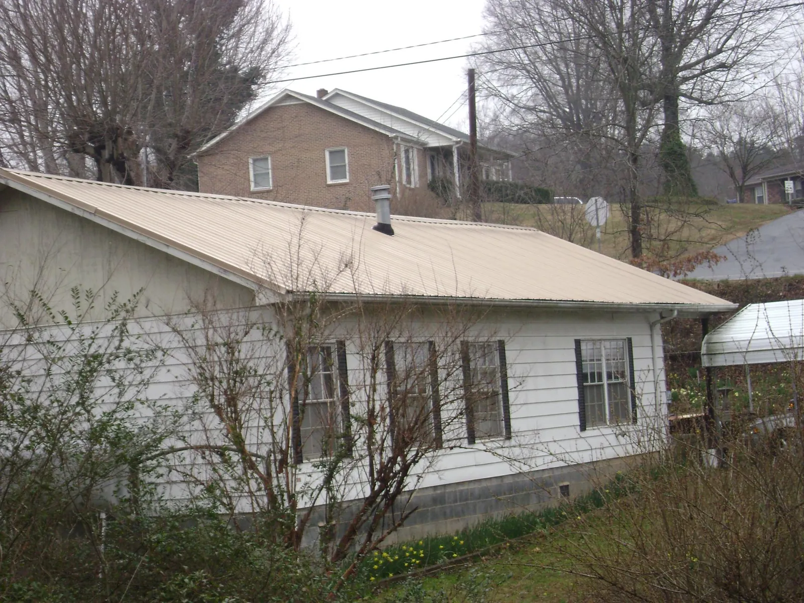 Tan metal roof on a white sided house set into a hillside — Commercial Roofing by Roofing Brothers in Ocean Gate